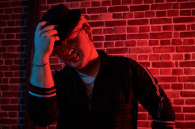 Gece kulübündeki rapçi çocuk. Modern giyimli, şık siyah şapkalı, sarı yuvarlak gözlüklü, kırmızı ışıkla aydınlatılmış tavan arası tarzı bir odada duran tombul bir adamın portresi. Erkeklerin gençlik tarzı.