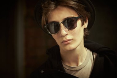 Siyah kapüşonlu, şapkalı ve güneş gözlüklü şık bir gencin şehir caddesinde dikilirken yakın plan fotoğrafı. Gençlik tarzı, moda.