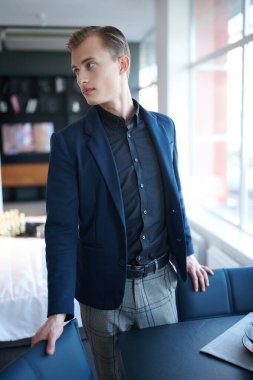 Modern bir ofiste duran şık takım elbiseli genç ve yakışıklı bir işadamının portresi. Ofis ve ev için iç mekan.