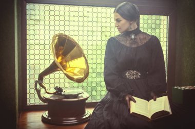 Siyah, sıkı siyah elbiseli, sırtı kıllı, genç ve güzel bir bayan elinde bir kitapla pahalı süslemelerle pencerenin kenarında sakince oturuyor. 19. yüzyıl tarzı. Tarihi roman..