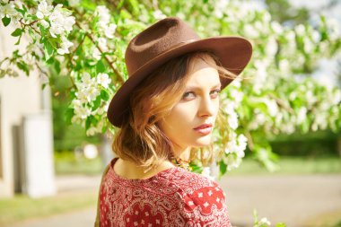 Güzellik ve moda. Hippi tarzı bluz ve şapkalı romantik bir kız çiçek açan ağaçların arasında duruyor. Boho ve hippi tarzı. Bahar mevsimi. 