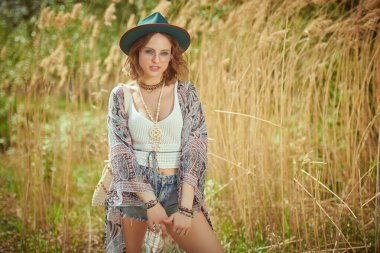 Boho tarzı kıyafetler ve aksesuarlarla süslü güzel bir kız sazlıkların arasında poz veriyor. Boho ve hippi tarzı. Tatil, seyahat. Boşluğu kopyala.