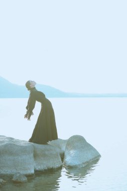 Siyah bir elbise içinde güzel, zarif bir kadın denizin kenarında duygularından muzdarip duruyor. 19. yüzyıl romanı.