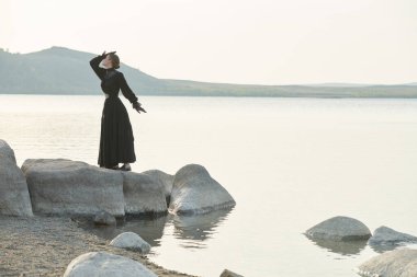Siyah bir elbise içinde güzel, zarif bir kadın denizin kenarında duygularından muzdarip duruyor. 19. yüzyıl romanı. Boşluğu kopyala.