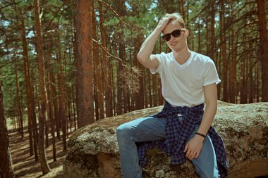 Turist yürüyüşçüsü çam ormanındaki taşların üzerinde dinlenmek için oturdu. Yürüyüş sırasında bir mola. Turizm, doğa keşfi. Yaz tatili. 