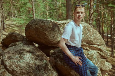 Turizm, doğa keşfi. Yürüyüş sırasında çam ormanında kayaların orada dinlenen yakışıklı bir yürüyüşçünün portresi. Aktif dinlenme, yürüyüş, macera.