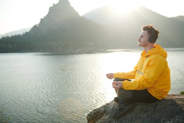 Doğayla uyum. Bir adam meditasyon yapar müzik dinler ve gün batımında dağdan güzel bir manzaranın tadını çıkarır. Seyahat, yaşam tarzı, rahatlama. Yaz tatilleri. Boşluğu kopyala.