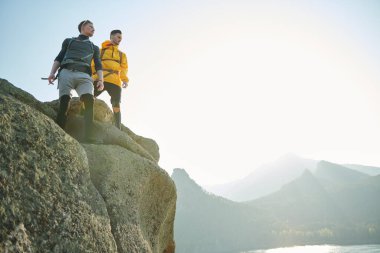 Bir dağın tepesinde duran ve güzel manzaraya bakan iki genç erkek dağcının portresi. Olağanüstü sporlar, dağ turizmi. Özgürlüğü ve başarıyı hissetmek. Boşluğu kopyala.
