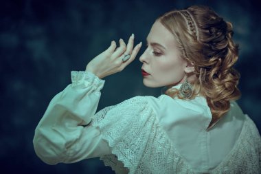 Zarif beyaz dantelli bir elbise içindeki güzel asil bir bayan esmer bir arka planda poz veriyor. Viktorya dönemi. Moda, saç stili ve makyaj. Tarihi roman..