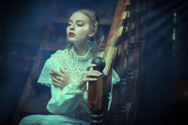 Beyaz dantelli elbiseli güzel bir bayan aristokrat karanlık bir odada tahta merdivenlerde oturuyor. Tarihsel mistik roman. Viktorya tarzı.