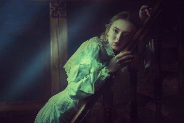Beyaz dantelli bir elbise içindeki güzel bir asil kadın, klasik bir karanlık dairede duruyor, açık bir sis ile örtülmüş, merdivenlere yaslanmış. Viktorya tarzı. Tarihi roman..