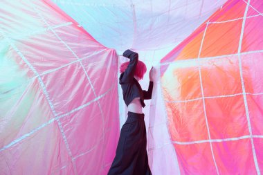 Paraşüt kumaşıyla çevrili siyah takım elbiseli, modaya uygun kızıl saçlı çekici bir manken. Yüksek moda. Saç stili, saç boyası.