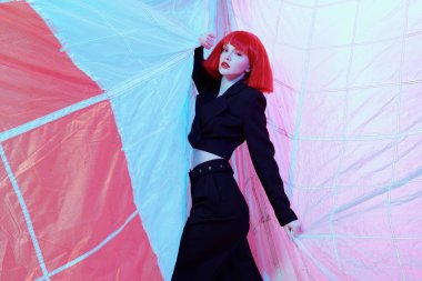 Paraşüt kumaşıyla çevrili şık siyah takım elbiseli, parlak kızıl saçlı güzel bir manken. Yüksek moda. Saç stili, saç boyası.