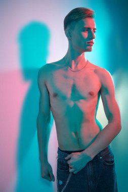 Kotlu, çıplak gövdeli çekici bir genç adam çok renkli ışıkta duvarın yanında duruyor. İnsanın güzelliği ve sağlığı. Resim..
