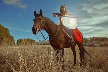Cesur kadın savaşçı Valkyrie elinde bir kılıç ve kalkanla savaş atının üzerinde oturuyor. İskandinav mitolojisi. Efsanevi fantezi.