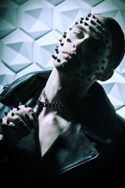 Siyah deri ceketli, yüzünde ve elinde metal çiviler olan beyaz bir teknolojide poz veren vahşi bir gencin portresi. Saldırgan bir moda.. 