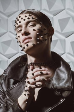 Agresif bir moda. Siyah deri ceketli, yüzünde ve elinde metal çiviler olan beyaz bir teknolojide duygusal olarak poz veren vahşi bir gencin portresi..