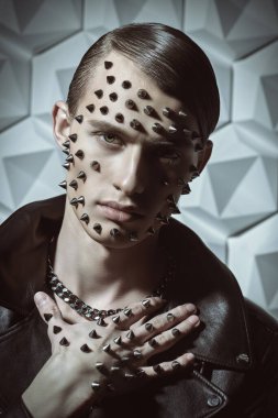 Yakışıklı bir erkek model siyah deri bir ceketle poz veriyor ve yüzünde ve elinde metal çiviler var. Saldırgan bir moda.. 