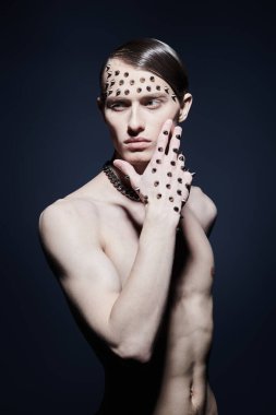 Çekici bir adamın portresi çıplak gövdesiyle yüzünde ve elinde metal çivilerle karanlık bir arka planda poz veriyor. Sanat ve erkek güzelliği.