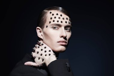 Çekici bir gencin portresi. Yüzünde ve elinde metal çiviler var. Arka planda poz veriyor. Sanat ve moda.