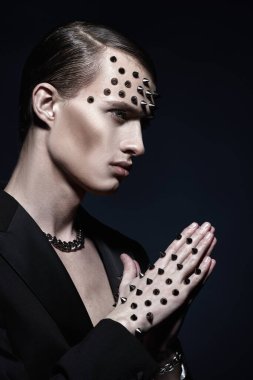 Yakışıklı, vahşi bir adam siyah bir ceketle poz veriyor. Yüzünde metal çiviler, elinde siyah bir arka plan var. Moda fotoğrafı.. 