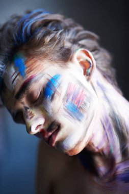 Sanat, moda ve vücut boyama. Rengarenk tenli yakışıklı bir sarışının yakın plan fotoğrafı. Karanlık bir arka planda, gözleri kapalı, huzur içinde duruyor.. 