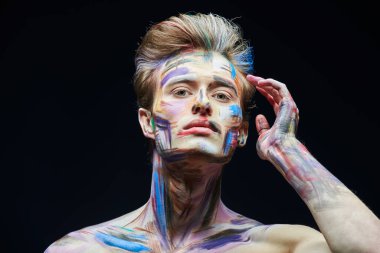 Sanat ve erkek güzelliği. Siyah bir arka planda duran renkli yüzlü yakışıklı bir adamın portresi..