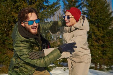 Güneşli bir günde, karlı bir kış parkında eğlenen iki neşeli genç arkadaş. İyi ruh hali, duygular. Kış aktiviteleri.  