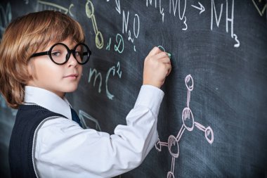 Zeki çocuklar. Düzgün okul üniforması ve gözlüklerle yakışıklı bir çocuk tahtada durup karmaşık kimyasal formüller yazıyor. Eğitim. 