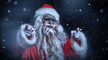 Korkunç bir zombi Noel Baba portresi. Gecenin bir yarısı kar altında durup işaret parmağını kameraya doğrultuyor. Noel 'de kabus. Cadılar Bayramı.