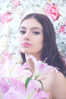 Çiçekler ve güzellik. Güzel, nazik bir kız narin beyaz ve pembe çiçeklerin arka planında zambak çiçekleriyle duruyor. Makyaj ve makyaj malzemeleri. Parfüm.