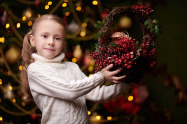 Beyaz kazaklı mutlu küçük bir kız elinde bir sepet tutuyor. Noel 'in şenlikli iç mimarisi. Noel hediyeleri ve dekorasyonlar. 