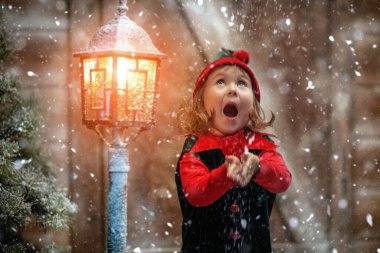 Kış Noel Masalı. Komik şirin bir elf kızı kar taneleri yakalar ve sevinir, karla kaplı ahşap bir kulübede ve fenerde durur..