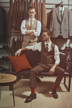 Fashionable men's clothing. Two well-groomed gentlemen in classic suits spend time in a premium men's clothing store choosing new clothes. clipart