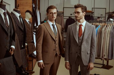 Zarif klasik takım elbiseli ve gözlüklü iki saygıdeğer adam prim erkek giyim mağazasında yan yana durur. İş stili. Erkek modası. 