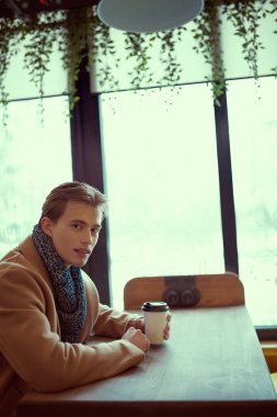 Soğuk bir kış gününde sıcacık bir kafede sıcak kahve içen şık, sarışın bir adamın portresi. İnsan konsepti, yaşam tarzı.