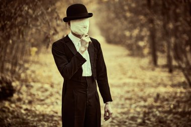 Yüzünde alçı bandajlı, melon şapkalı ve siyah ceketli tuhaf ve ürpertici bir beyefendi eski bir sonbahar parkında duruyor. Cadılar Bayramı. Eski tarz. Korku, gerilim.