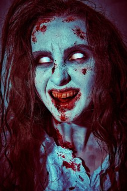 Şeytan tarafından ele geçirilmiş biçimsiz kanlı bir kadın solgun gözlerle kameraya bakar ve güler. Zombi kadın. Korku, gerilim. Cadılar Bayramı. 