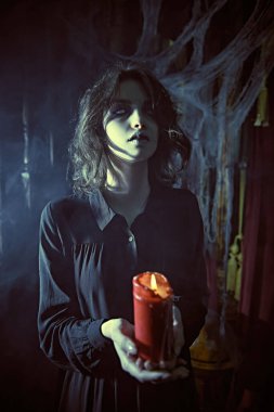 Siyah yas elbisesi giymiş yalnız bir hayalet kız elinde mumla karanlık, kasvetli bir odada duruyor, örümcek ağlarıyla örtülü. Korku filmi, gerilim. Cadılar Bayramı.