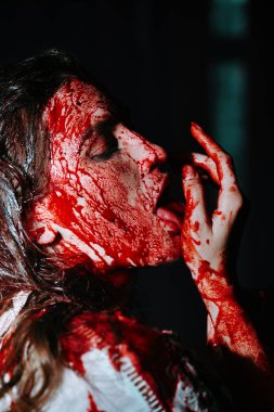 Spooky portrait of a girl drenched in blood standing in a dark gloomy castle licking blood from her body. Horror, thriller. Halloween. Vampires. clipart