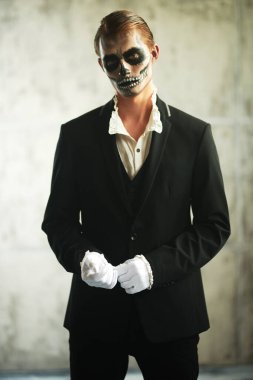 Cadılar Bayramı. Kafatası makyajlı yakışıklı bir adamın portresi zarif siyah bir takım elbise ve grunge arka planda klasik beyaz gömlek içinde duruyor. Dia de los muertos. Ölülerin Günü. 