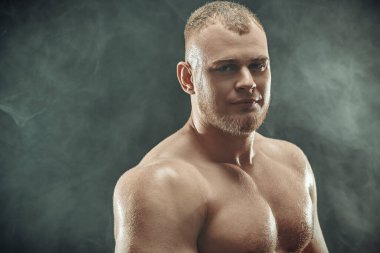 Duman dolu karanlık bir arka planda poz veren güçlü, sağlıklı, yakışıklı bir atletin portresi. Erkek güzellik konsepti. Fitness, vücut geliştirme.