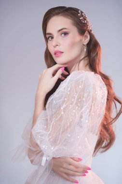 Zarif beyaz gelinlik içinde güzel bir gelinin stüdyo fotoğrafı. Gri bir arkaplanda stüdyo resmi. Düğün makyajı ve saç stili. 