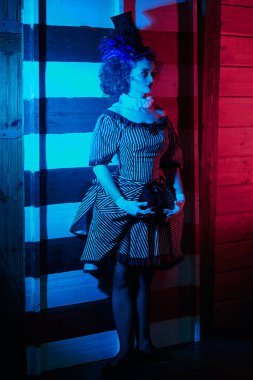 Karanlık sirk konsepti. Palyaço kostümlü bir sirk sanatçısı bıçak fırlatma numarası yapar. Retro biçimi.