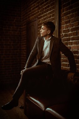 Takım elbiseli şık, orta yaşlı bir adam loş ışıklandırmalı bir çatı katındaki deri bir koltukta düşünceli bir şekilde oturur. Erkek güzelliği, moda. Yaşam biçimi.
