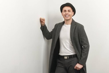 Beyaz bir duvarın yanında duran ve gülümseyen zarif ceketli, orta yaşlı yakışıklı bir adamın portresi. Erkek güzelliği, moda. Yaşam tarzı. Hippi adam. Boşluğu kopyala.