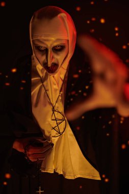 Avına elini uzatan cehennem ateşi kıvılcımlarıyla çevrili kızgın şeytani dişleri olan bir rahibenin portresi. Cadılar Bayramı ve Dehşet.