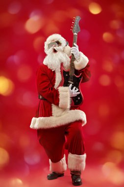 Güneş gözlüklü ve kulaklıklı Noel Baba gitar çalıyor ve duygusal olarak şarkı söylüyor. Mutlu noeller. Parti zamanı. Tam yol ileri. Parlak ışıkları olan kırmızı arkaplan. 