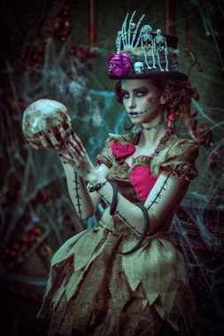 Voodoo büyüsü. Esrarengiz ve korkutucu bir kızın portresi voodoo bebeği gibi giyinmiş, kasvetli eski bir evde örümcek ağlarıyla kaplanmış ve elinde bir kafatası tutan. Cadılar Bayramı.