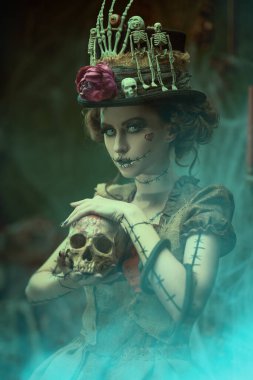 Voodoo büyüsü. Esrarengiz ve korkutucu bir kızın portresi voodoo bebeği gibi giyinmiş, kasvetli eski bir evde örümcek ağlarıyla kaplanmış ve elinde bir kafatası tutan. Cadılar Bayramı.